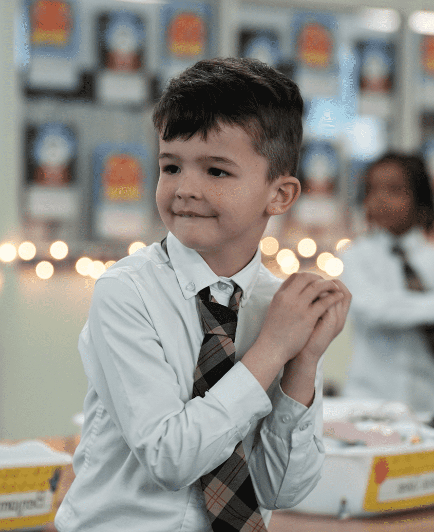 Young boy in a white shirt and tie clapping at a classroom event