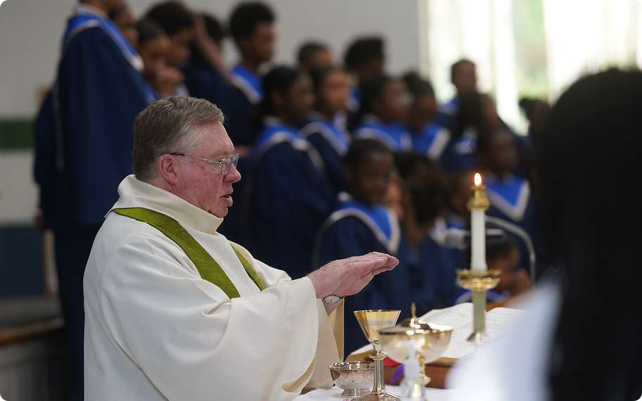 A priest celebrating Mass at the altar with choir members in the background