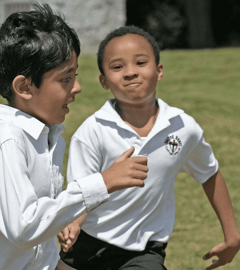 Two boys in white school uniforms running outdoors on a grassy field