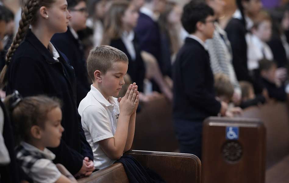 Children standing and sitting in a church pew, one boy praying with hands clasped