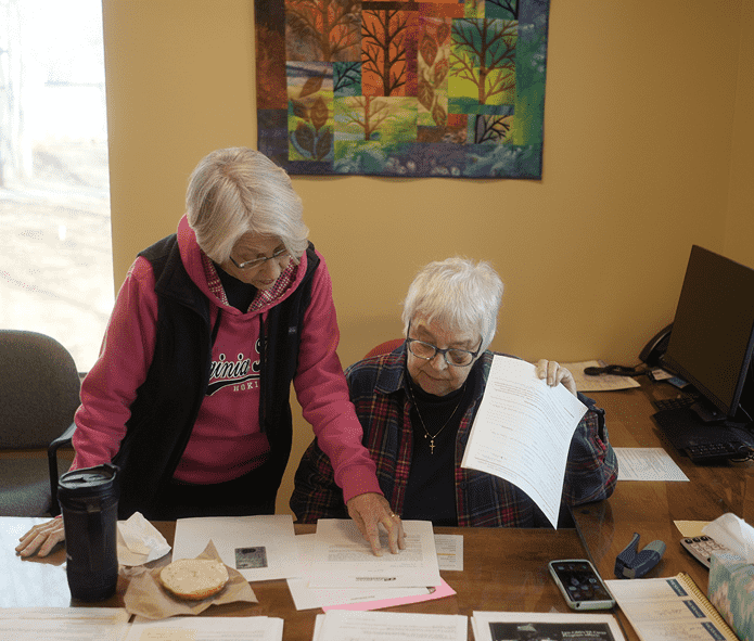 Two women reviewing paperwork at a desk, one pointing to a document while the other holds a page