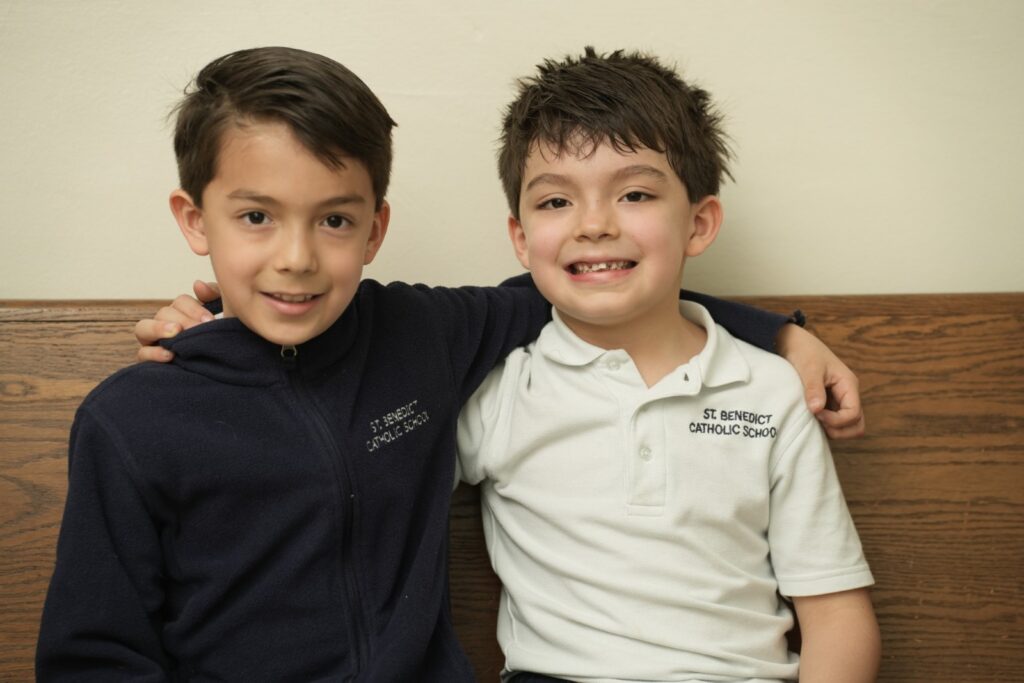 Two boys in school uniforms sitting together with their arms around each other